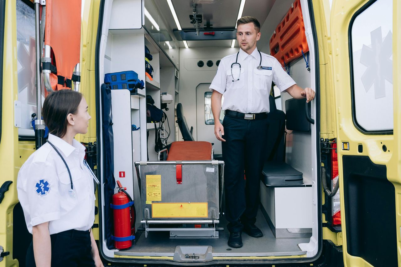 Two paramedics in uniforms and stethoscopes preparing ambulance for upcoming medical emergencies.